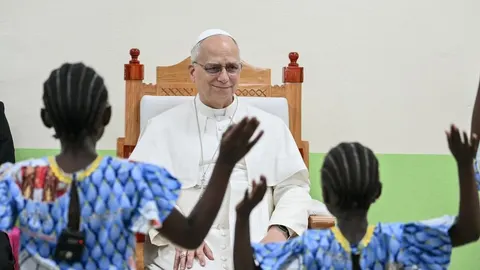 Papa Franjo sjedi i gleda djecu iz Afrike koja dižu ruke u znak pozdrava.