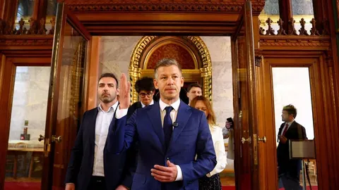 Peter Magyar u plavom odijelu podiže ruku ispred ulaza u zgradu parlamenta.