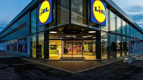 Moderna zgrada Lidl marketa s velikim staklenim izlozima i osvijetljenim logotipom.