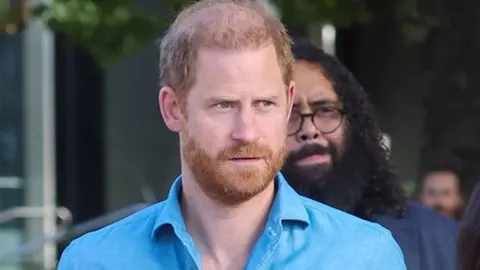 Princ Harry u plavoj košulji ozbiljnog izraza lica