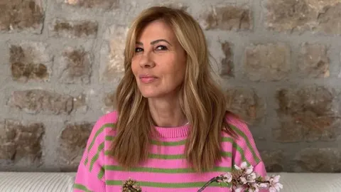 Mirna Zidarić u ružičasto-zelenom pletenom džemperu ispred kamenog zida.