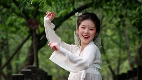 Nasmijana žena u tradicionalnoj bijeloj kineskoj odjeći pleše u prirodi