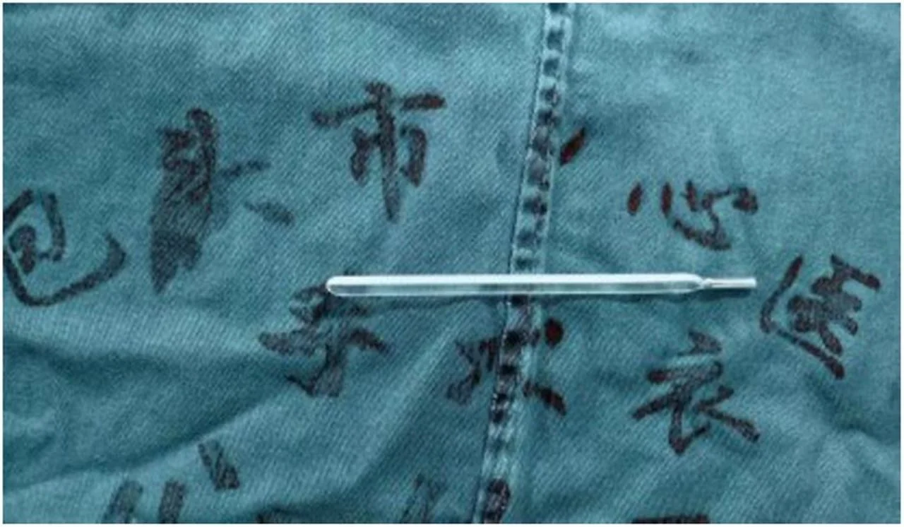 Stakleni toplomjer položen na zelenu tkaninu s tragovima kineskih znakova.