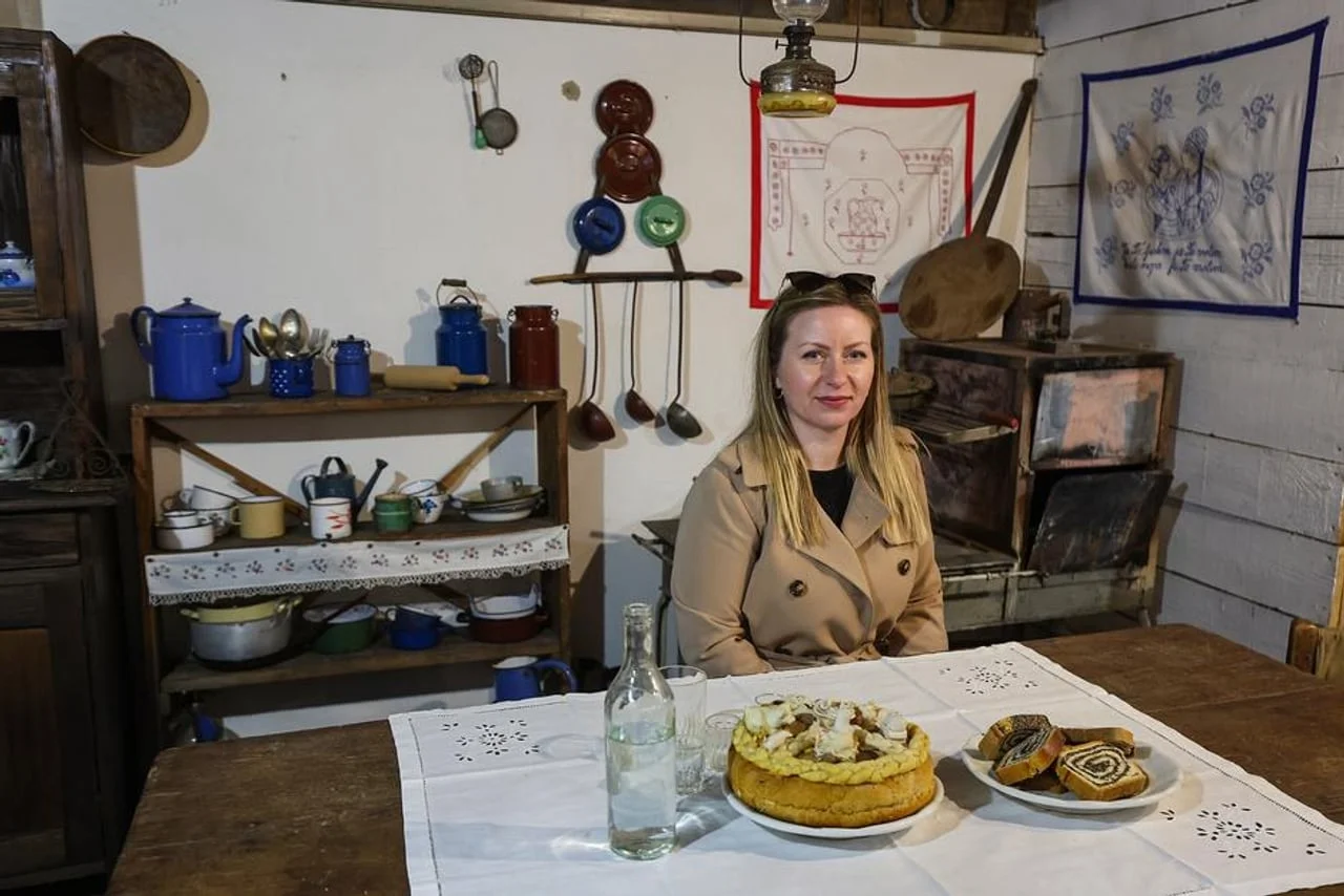 Žena sjedi za drvenim stolom s tradicionalnom masnicom u starinskoj kuhinji.