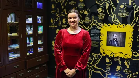 Žena u crvenoj haljini stoji ispred zida s ilustracijama bajki u Ogulinu.