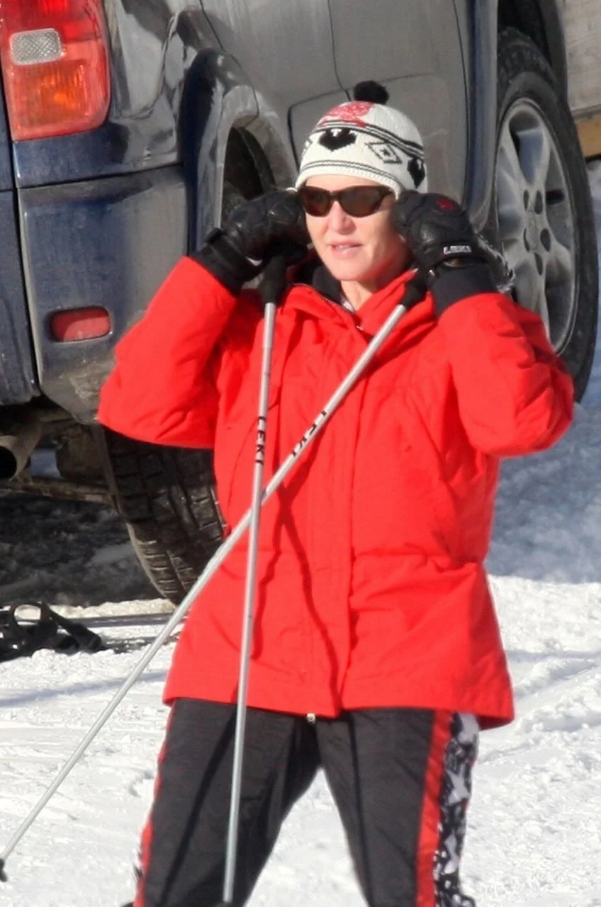 Žena u crvenoj skijaškoj jakni s naočalama i kapom na snijegu