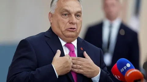 Viktor Orbán u tamnom odijelu s ružičastom kravatom govori pred mikrofonima.