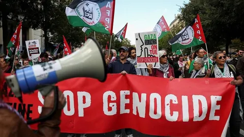 Prosvjednici drže veliki crveni transparent i palestinske zastave na ulici.