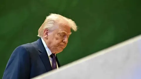 Donald Trump u odijelu s pognutom glavom ispred zelene pozadine