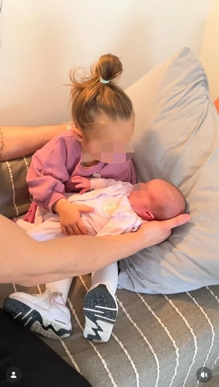 Djevojčica nježno drži novorođenče na jastuku uz pomoć odrasle osobe.