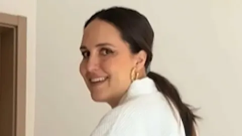 Nasmiješena Lana Jurčević u bijelom ogrtaču stoji pored dječjeg krevetića u rodilištu.