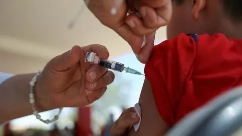 Medicinska sestra daje cjepivo u nadlakticu djeteta u crvenoj majici.