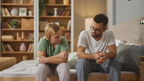 Zabrinuti muškarac i žena sjede na rubu kreveta u spavaćoj sobi.