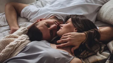 Muškarac i žena leže zagrljeni u krevetu pod bijelim plahtama.