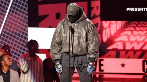 Kanye West s maskom na licu i kapuljačom stoji na pozornici tijekom nastupa.