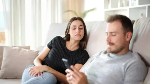 Žena sumnjičavo gleda u pametni telefon koji muškarac drži dok sjede na kauču.