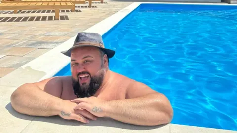 Jacques Houdek sa šeširom nasmiješen u bazenu na sunčanom danu