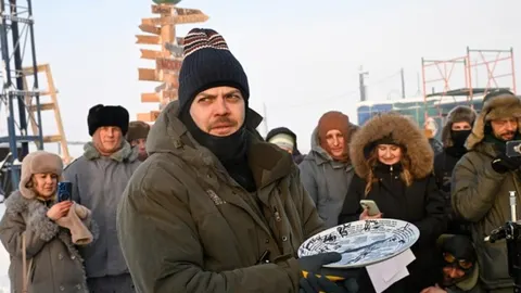 Muškarac u zimskoj odjeći drži ukrasni tanjur ispred skupine ljudi na Arktiku.