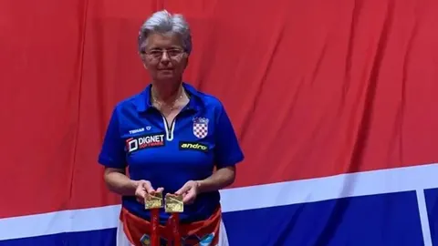 Branka Batinić u plavom dresu s medaljama ispred hrvatske zastave.