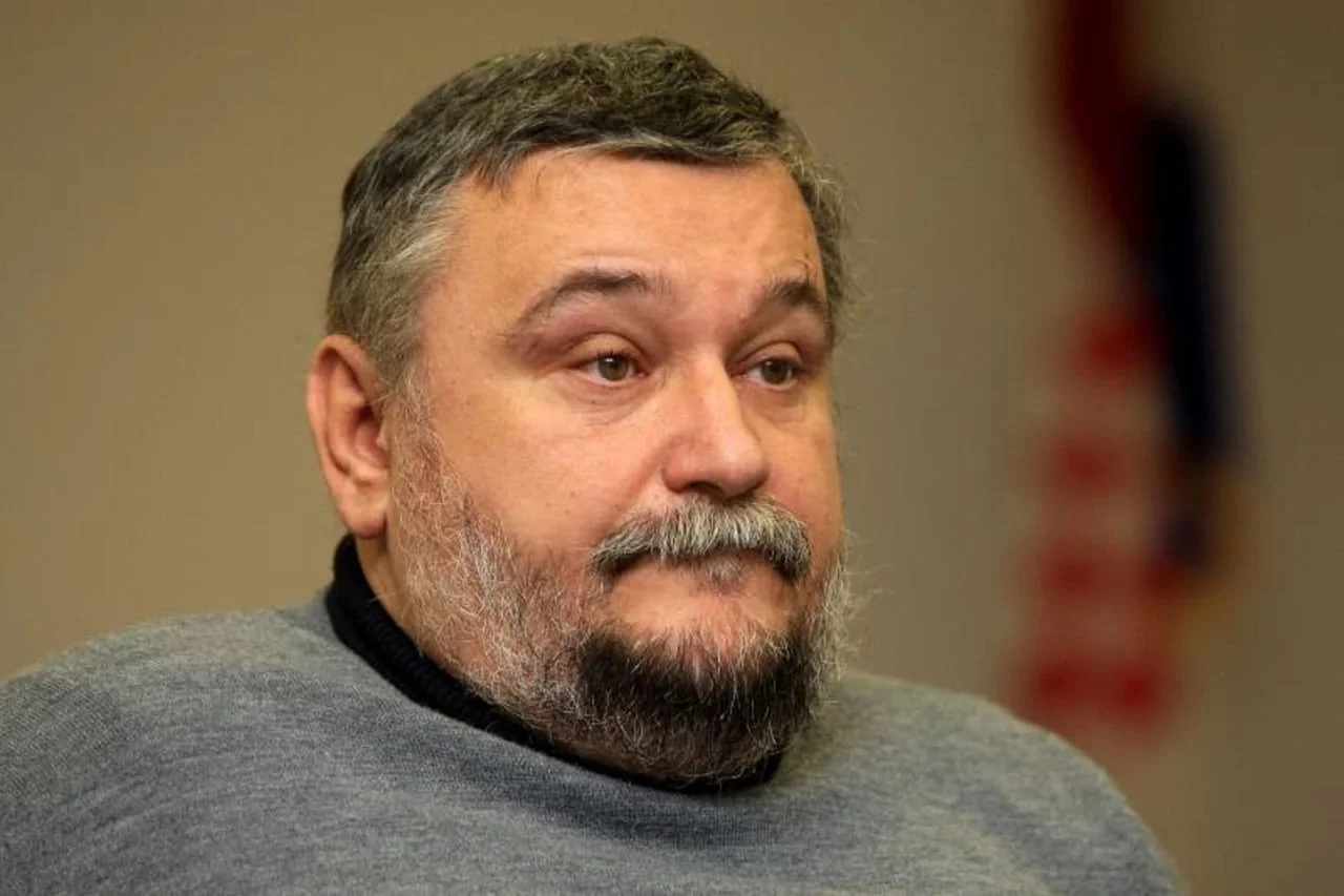 Portret muškarca srednjih godina sa sijedom bradom u sivoj majici.