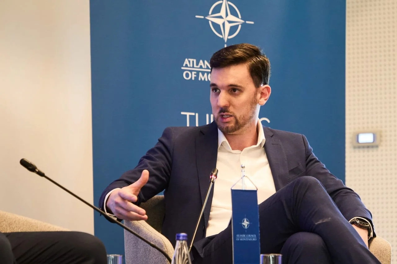 Muškarac u plavom odijelu govori na panel raspravi ispred NATO logotipa.