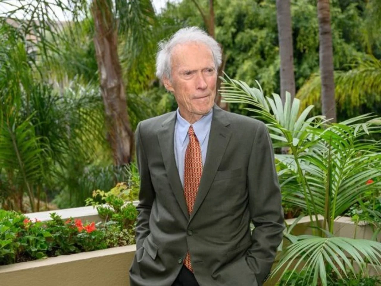Stariji Clint Eastwood u maslinastom odijelu ispred tropskog bilja