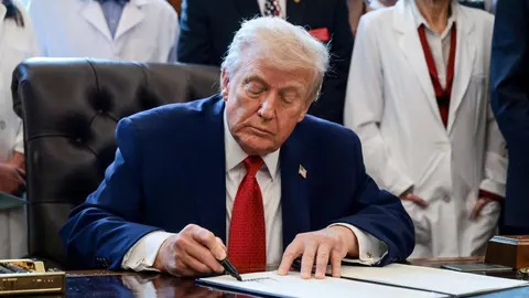 Donald Trump u tamnom odijelu potpisuje službeni dokument za radnim stolom.