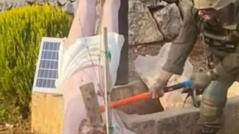 Vojnik u uniformi zamahuje čekićem prema donjem dijelu bijelog kipa na otvorenom.