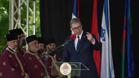 Aleksandar Vučić govori za govornicom dok iza njega stoje crkveni dostojanstvenici.