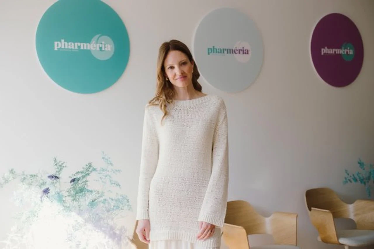 Žena u bijelom pletenom džemperu stoji ispred Pharmeria natpisa.