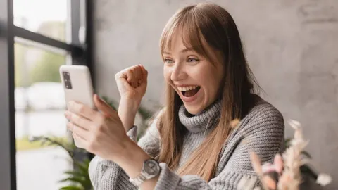 Nasmijana žena s mobitelom u ruci slavi dobre vijesti