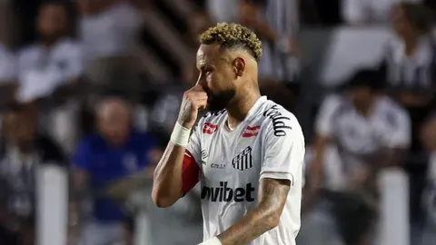 Neymar u bijelom dresu Santosa briše lice rukom na nogometnom terenu.