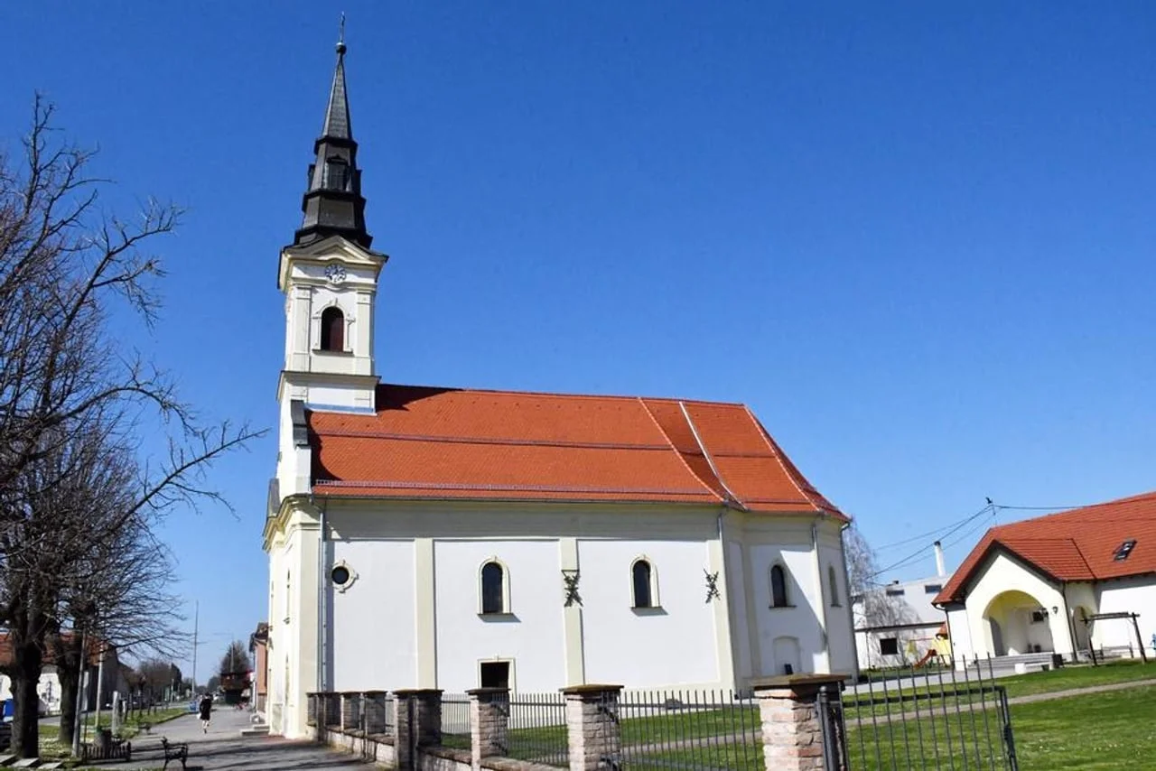 Bijela katolička crkva s visokim zvonikom pod plavim nebom