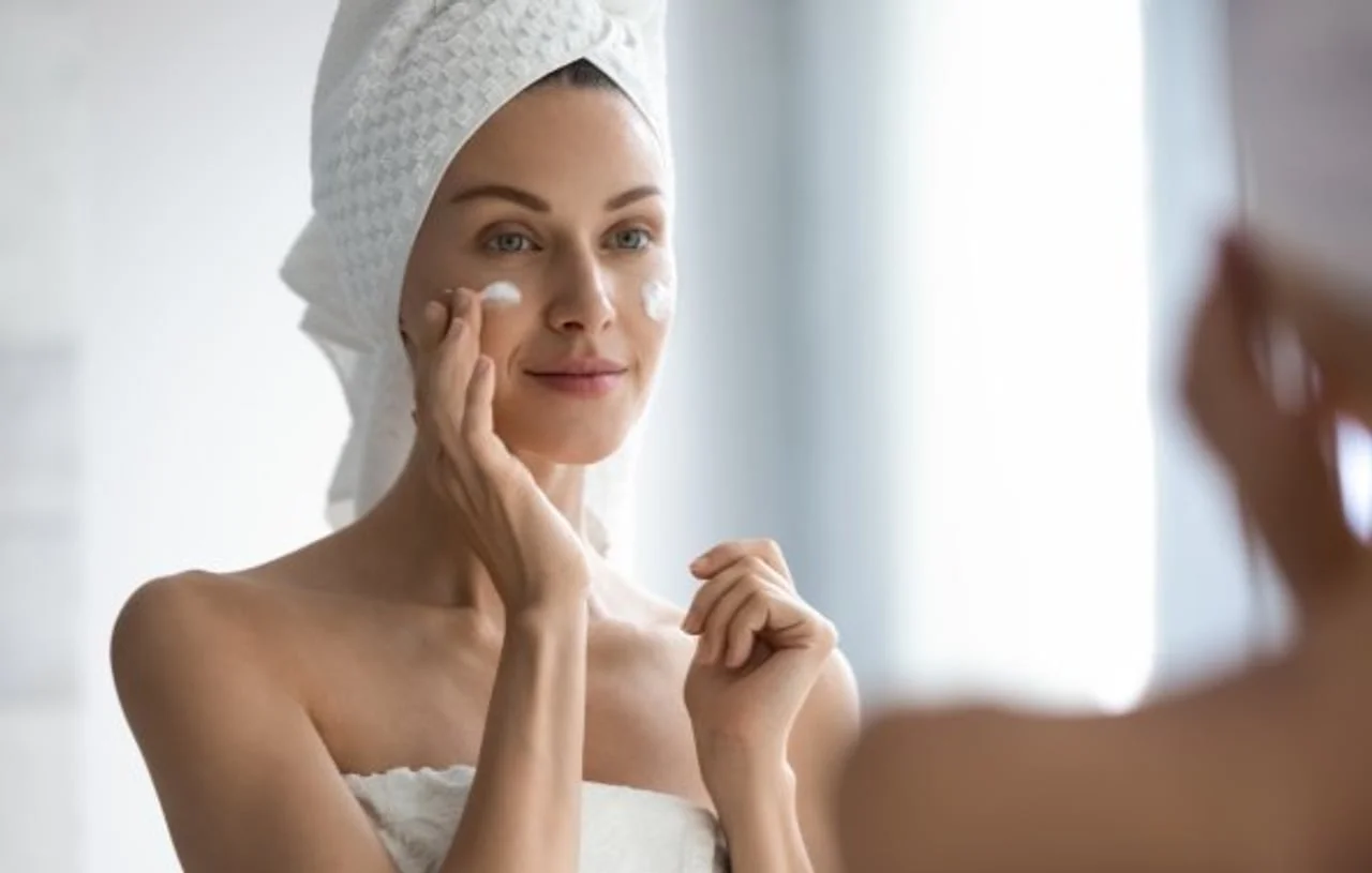 Žena s ručnikom na glavi nanosi hidratantnu kremu na lice