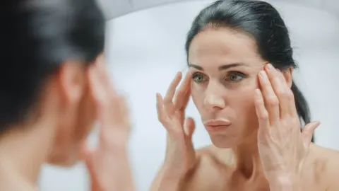 Žena promatra bore na licu ispred ogledala