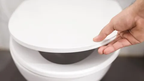 Ruka spušta bijeli poklopac wc školjke u kupaonici