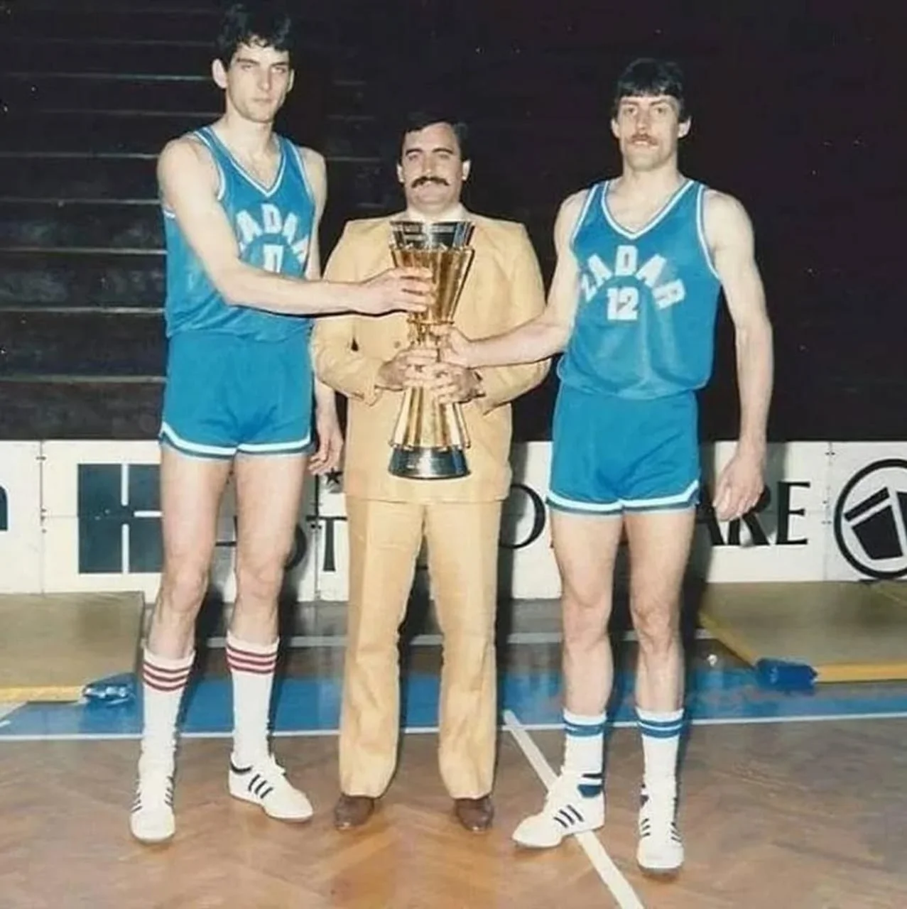 Vlade Đurović u odijelu stoji između dva košarkaša Zadra koji drže pehar
