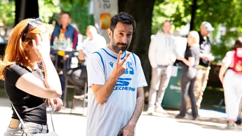 Glumac Asim Ugljen u sportskom dresu s bradom pokazuje znak mira na otvorenom.