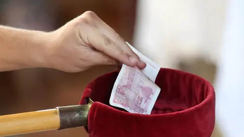 Ruka vjernika spušta novčanicu od 20 kuna u baršunastu košaricu za milodare.