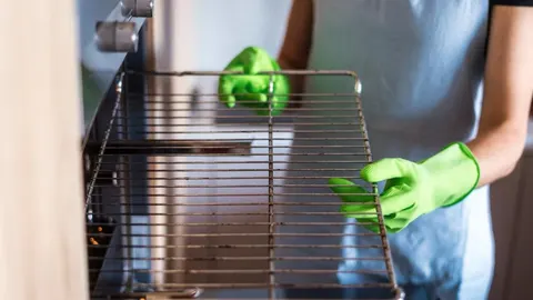 Osoba u zelenim rukavicama vadi rešetku iz pećnice radi čišćenja.