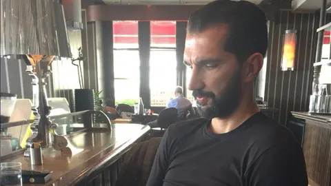 Portret Peđe Stojakovića iz profila u crnoj majici dok sjedi u interijeru restorana.