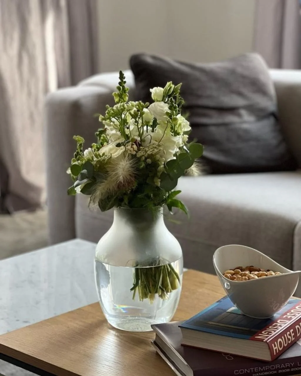 Buket bijelog cvijeća u staklenoj vazi na stolu uz knjige o dizajnu.