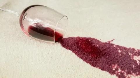 Proliveno crno vino iz čaše na svijetlom tepihu