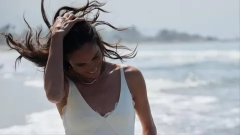 Meghan Markle nasmiješena na plaži s kosom na vjetru