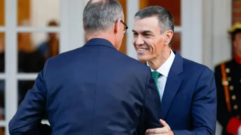 Pedro Sanchez se smiješi i rukuje s muškarcem u tamnom odijelu ispred zgrade.