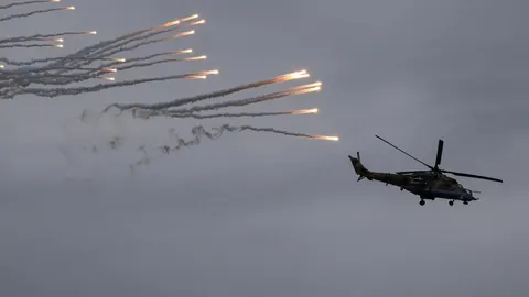 Vojni helikopter ispaljuje toplinske mamce na sivom nebu tijekom vježbe.