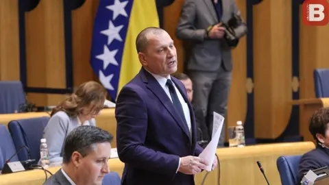 Zlatko Miletić govori za govornicom s papirima u rukama ispred zastave BiH.