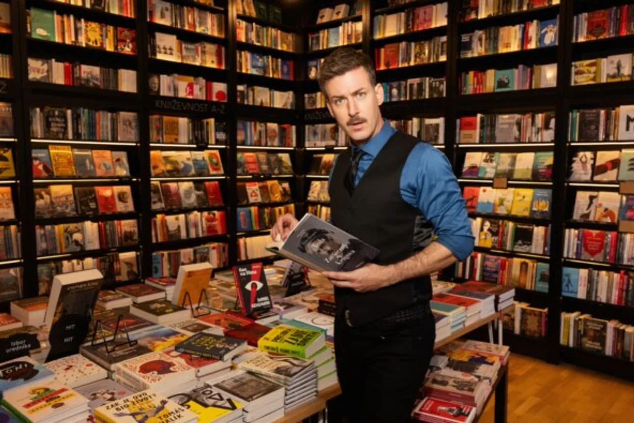 Glumac Matija Kačan stoji u knjižari okružen policama s knjigama.