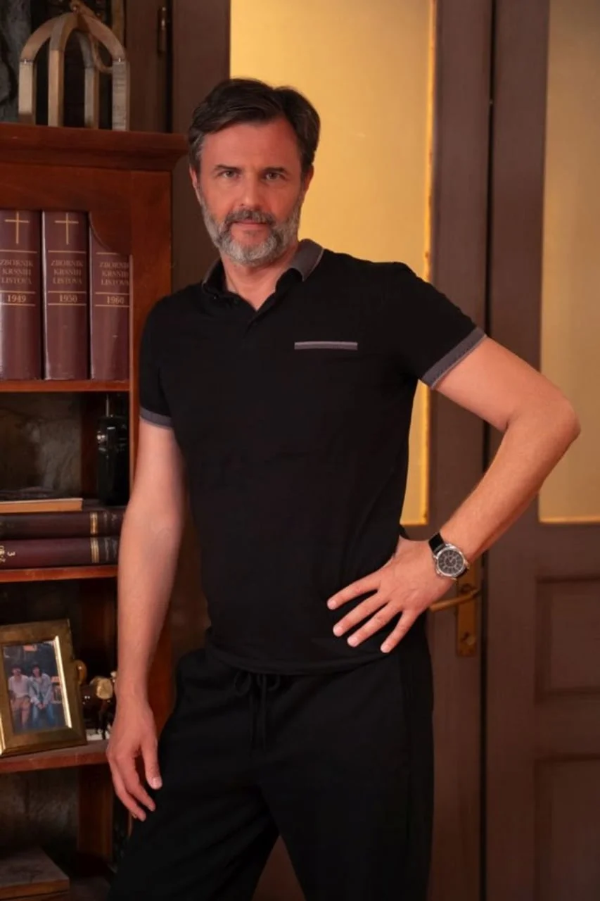 Portret Vladimira Posavca Tušeka u crnoj majici pored police s knjigama