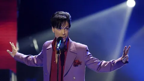 Prince u ljubičastom odijelu nastupa na pozornici pod reflektorima.